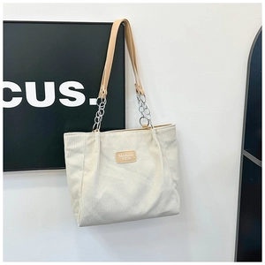 Detail of white corduroy tote bag with leather logo patch and metal chain strap