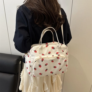 White corduroy strawberry tote bag with handles and crossbody strap on female model