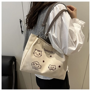 Detail of canvas tote bag with cat illustrations and brown leather straps on a shoulder