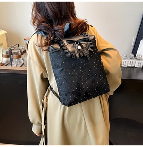 Détail du sac à dos noir avec bordure en dentelle, nœud papillon et breloque en perle