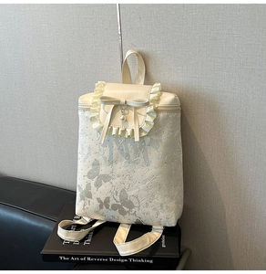 Détail macro du sac à dos crème avec imprimés papillons et bordures en dentelle plissée