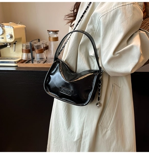 Détail du sac demi-lune noir brillant avec bandoulière chaîne et breloque sphérique