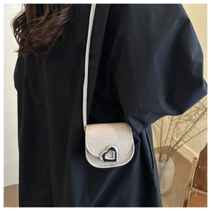Gros plan du mini sac crème en cuir texturé avec fermoir cœur doré et bandoulière élégante