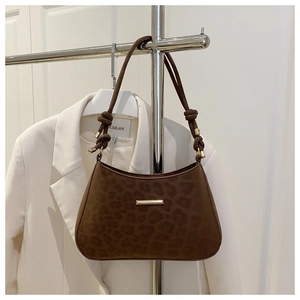 Detail of leopard print underarm bag featuring a gold metal bar and knotted shoulder strap