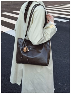 Close-up of a large dark brown PU leather tote bag with a fashion logo on a beige coat