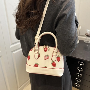 White shell bag with strawberry print and gold hardware worn as crossbody fashion accessory