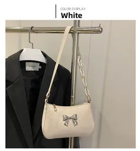 Close-up of a white leather underarm bag featuring a silver metal bow and chain strap