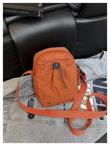 Détail du sac bandoulière orange en nylon avec poche à cordon et broderie de marque