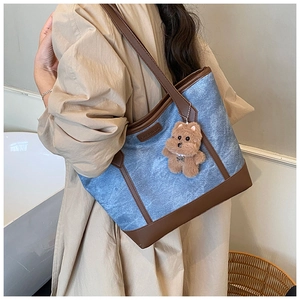 Detail of denim and leather tote bag with FASHION label and plush bear pendant