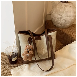 Detail of beige tote bag with brown leather straps, FASHION label and plush dog charm