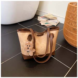 Detail of beige tote bag with brown leather trim and cute teddy bear charm accessory