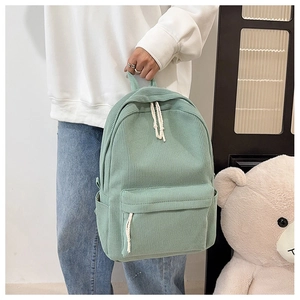 Detail of corduroy backpack in sage green featuring front zipper pocket and side slots