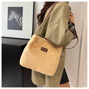 Détail du sac cabas en peluche beige avec bandoulière en cuir marron et étiquette latérale