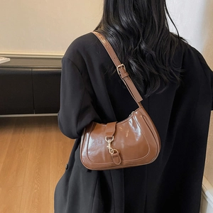 Brown glossy leather crescent underarm bag worn by model over a black blazer jacket