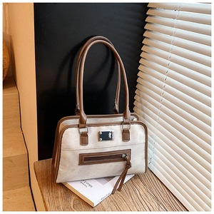 Close-up of vintage beige tote bag with brown trim and silver metal plaque on wood surface