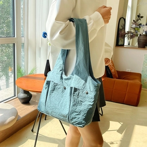 Light blue large capacity tote bag with dual front pockets shown on shoulder in sunlight