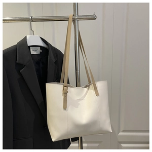 Detail of cream tote bag with brown straps, fashion lettering, and adjustable buckle