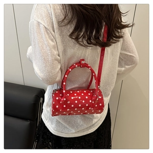 Macro shot of a red polka dot barrel bag worn crossbody by a model for size and fit view