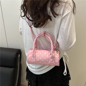 Chic pink polka dot barrel bag in glossy patent leather with top handles and strap