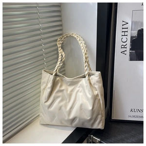 Detail of cream tote bag featuring textured diagonal embossing and woven dual straps
