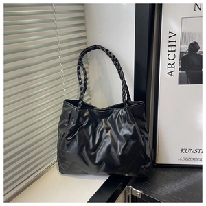 Detailed view of black pleated leather tote bag with braided handles on a minimalist table