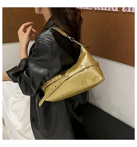Detail view of a metallic gold half-moon shoulder bag with buckle strap on a female model