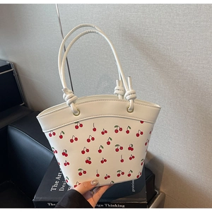 Dettaglio borsa in pelle bianca con stampa ciliegie, manico annodato e occhielli metallici