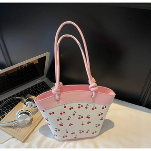 Dettaglio della borsa tote con stampa ciliegia e manici rosa su una scrivania ordinata