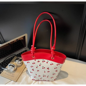 Dettaglio di una borsa tote bianca con stampe di ciliegie e manici in pelle rossa