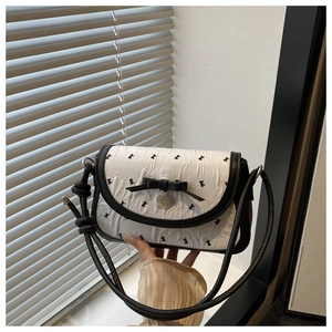 Close-up of heart-shaped metal pendant and bow detail on bicolor crossbody bag