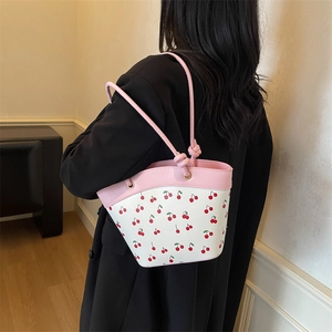 Borsa a secchiello rosa e bianca con stampa ciliegia e manico a nodo su una modella