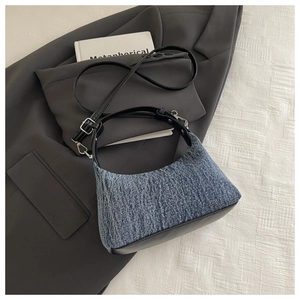 Detail of blue denim hobo bag with black leather trim on minimalist fabric background