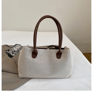 Detail of a minimalist canvas tote bag featuring premium brown leather handles and rich texture