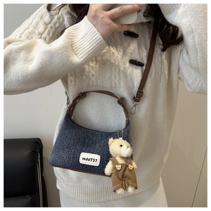 Détail du sac bandoulière en denim avec bandoulière en cuir brun et charm ours en peluche