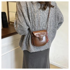 Gros plan d'un sac besace marron en cuir avec logo ovale embossé sur un pull gris chiné