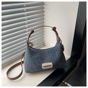 Detail of blue denim square bag featuring brown leather strap and brand logo patch
