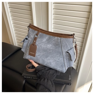 Detail van grijze canvas tas met bruine lederen bies en modieuze hanger op de bank