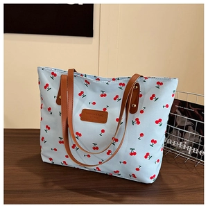 Détail du sac cabas bleu clair à imprimé cerises avec poignées et plaque en cuir brun