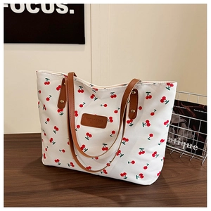 Détail du sac cabas en toile avec motifs cerises rouges et anses en cuir marron