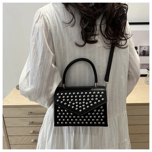 Close-up of black studded crossbody bag with silver hardware on a female model