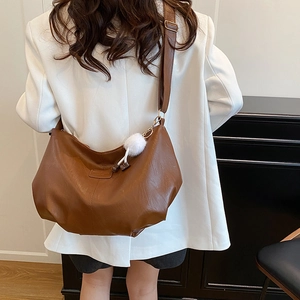 Brown large capacity tote bag with adjustable strap and white pompom on woman in white blazer