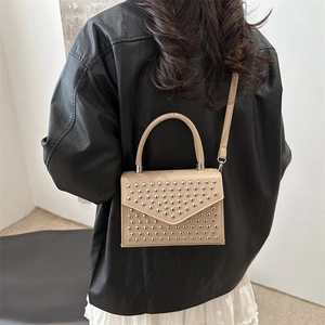 Beige rivet crossbody bag with metal studs and curved handle shown on female model