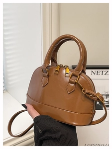 Detailed view of brown glossy leather shell bag with gold zippers and detachable strap