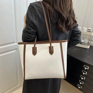 White woven tote bag with brown leather trim shown in a stylish minimalist interior