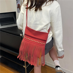 Fashionable red crossbody bag with golden studs and long tassels on white top model