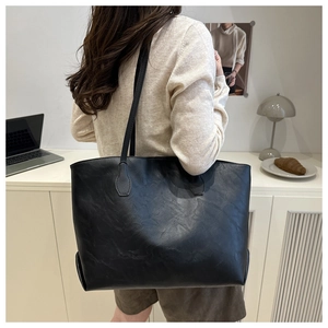 Detail of a black PU leather tote bag with long straps shown in a home office setting