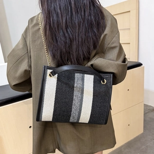 Striped woven tote bag with black leather handles and gold chain strap shown on shoulder