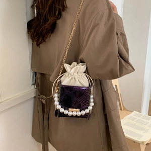 Detail of purple snake print bucket bag with pearl handle and chain strap on person