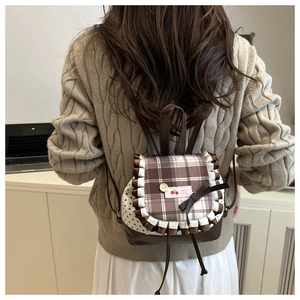 Detail of a mini backpack featuring plaid fabric, cherry embroidery, and ruffles