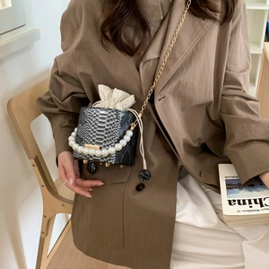 Chic snake-pattern bucket bag with pearl handle and gold chain strap worn by model